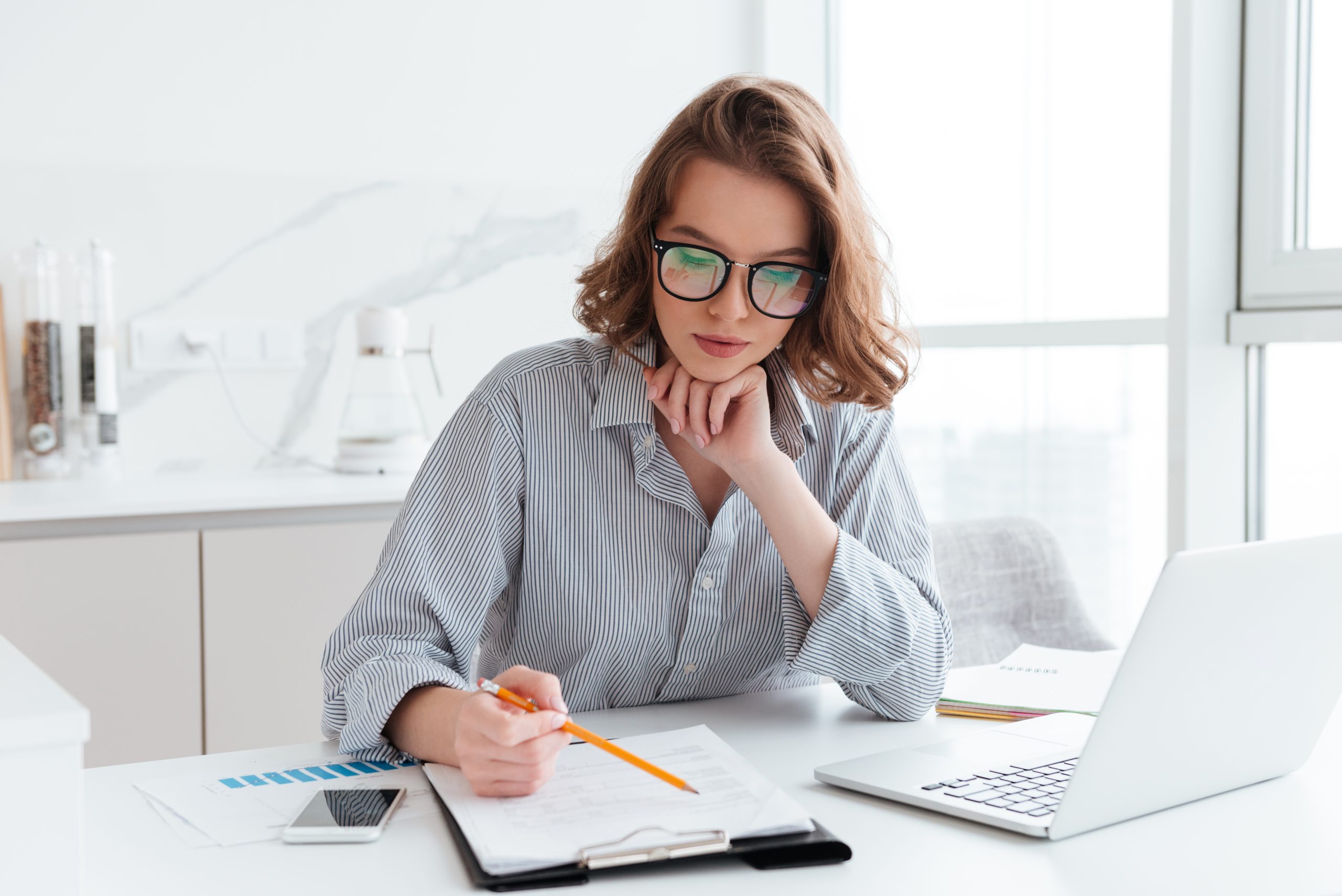 mlody skoncentrowany bizneswoman w szklach i pasiastej koszula pracuje z papierami w domu